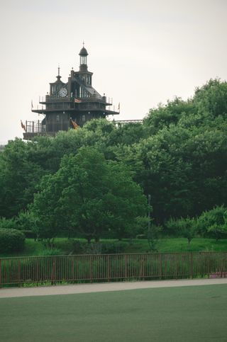 A tall brown building with a clocktower and spire in the distance rising above a forest