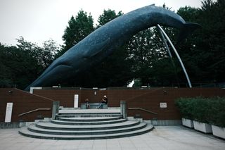 A woman and child sit on a bench beneath a life-sized model of a blue whale