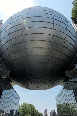 A large sphere suspended between two skyscrapers; the planetarium at the science museum in Nagoya, Japan
