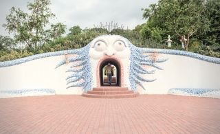 An entryway in a white wall that is shaped like an open mouth in a face with bulging, wild eyes, and blue, unkempt hair