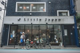 A woman stands in front of a building with a blue tile facade underneath a sign that reads “Little Japan”