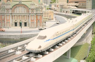 A Lego Shinkansen rides along some tracks in front of an elaborate Lego building