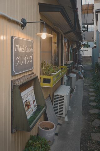 A sign reading “Miho's Kitchen” in English and Japanese on the side of a building in a small alley