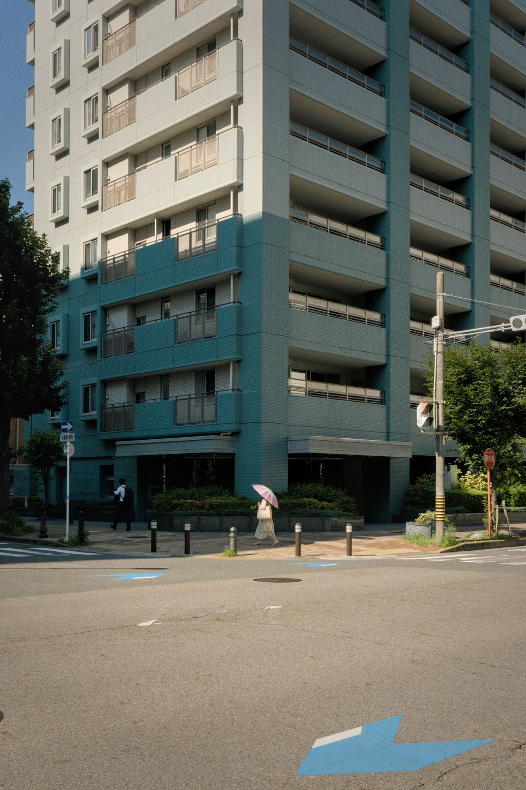 A person with an umbrella walks in front of a tall building on a street corner
