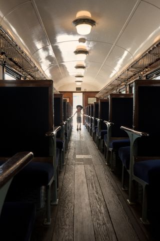 A little boy is backlit and framed by the door to an old train car at the far end of the aisle in the car